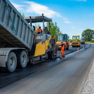 Reconstruction of the road, Tyumen, Russia: July 31, 2018. Dump truck unloads the asphaltic concrete mix in the paver. Roller compacts asphalt